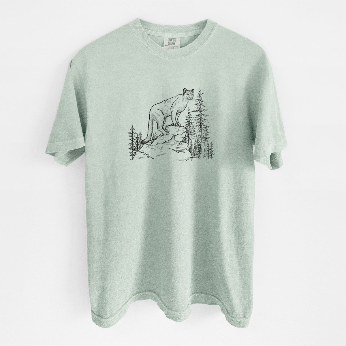 Bay green Comfort Colors t-shirt laid flat, printed with a black ink illustration of a mountain lion standing on a rocky ledge among pine trees.