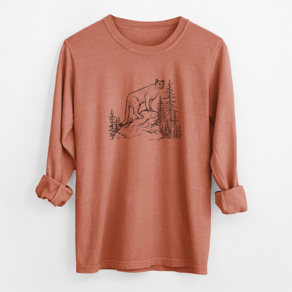 Yam burnt orange Comfort Colors long sleeve shirt laid flat with the cuffs rolled, printed with a black ink illustration of a mountain lion standing on a rocky ledge among pine trees.