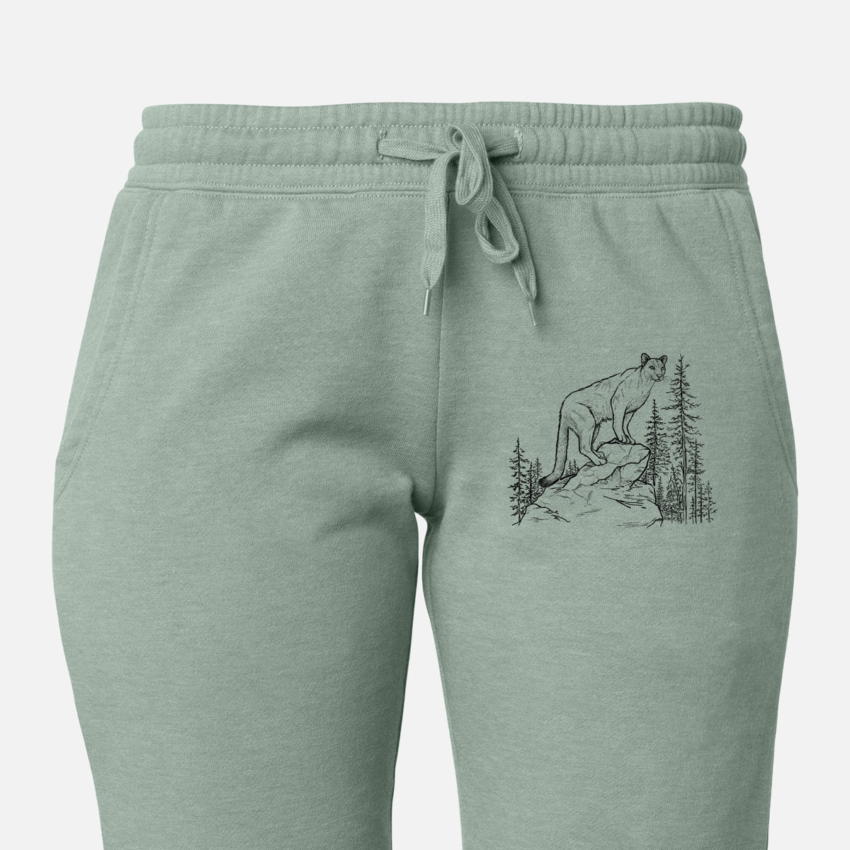 Front of sage green Cali Wave sweatpants, printed with a black ink illustration of a mountain lion standing on a rocky ledge among pine trees on the leg.