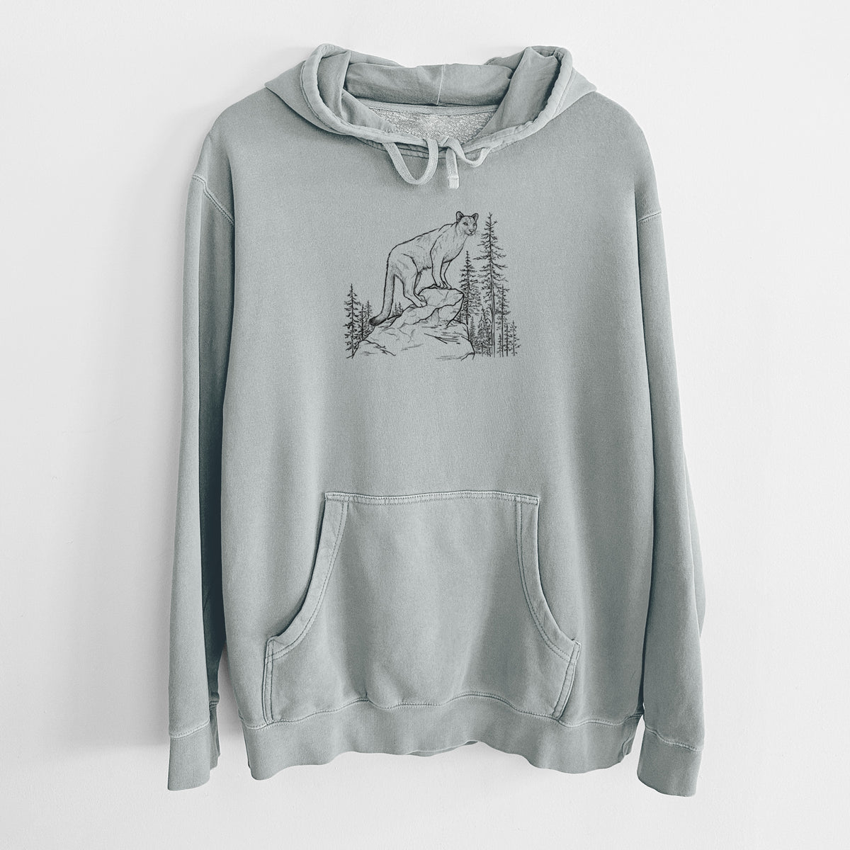 Sage green pigment dyed hoodie laid flat, printed with a black ink illustration of a mountain lion standing on a rocky ledge among pine trees.