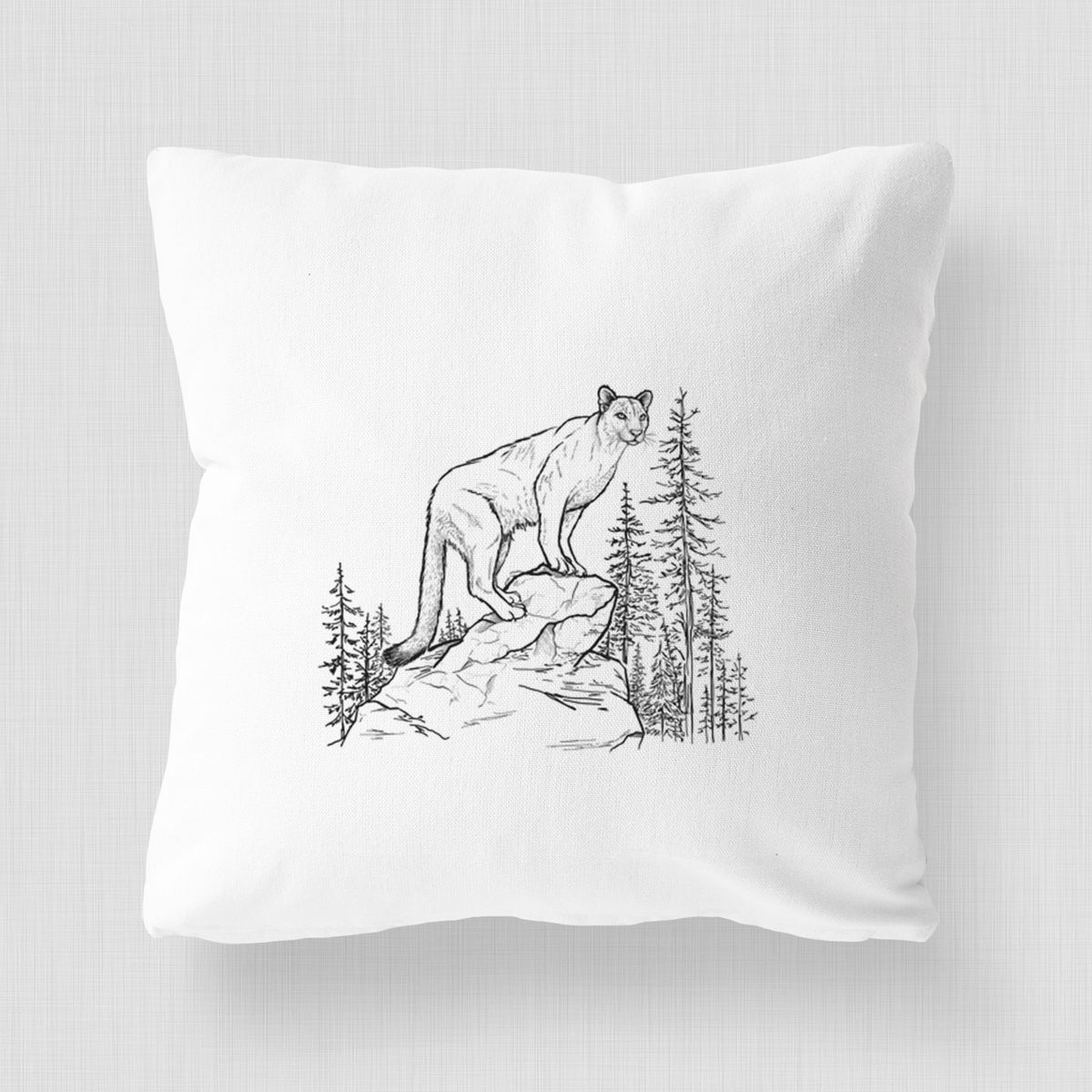 White pillow cover printed with a black ink illustration of a mountain lion standing on a rocky ledge among pine trees.