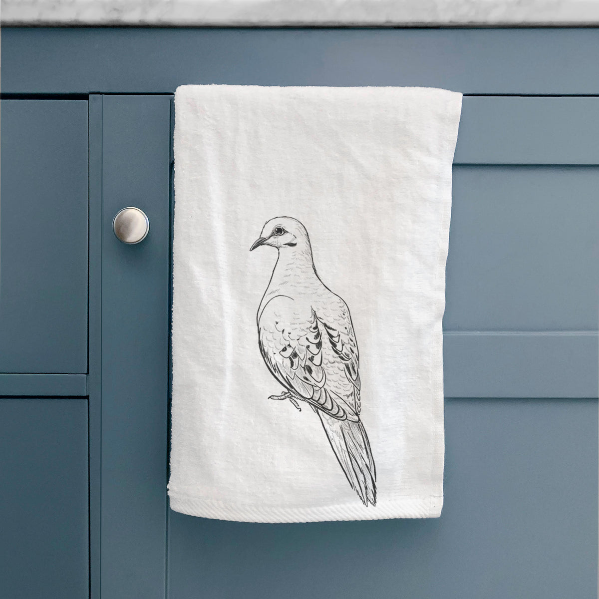 White hand towel printed with a detailed black ink sketch of a mourning dove perched, hanging on a cabinet door.