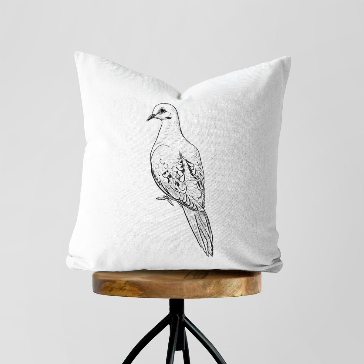White pillow cover printed with a detailed black ink sketch of a mourning dove perched, on a wooden stool.