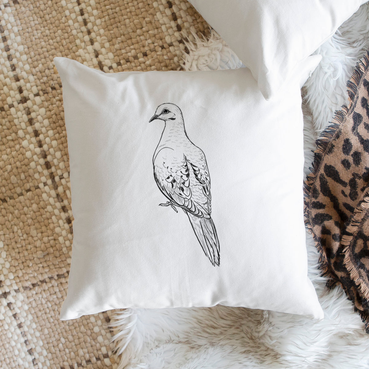 White pillow cover printed with a detailed black ink sketch of a mourning dove perched, on a woven chair.