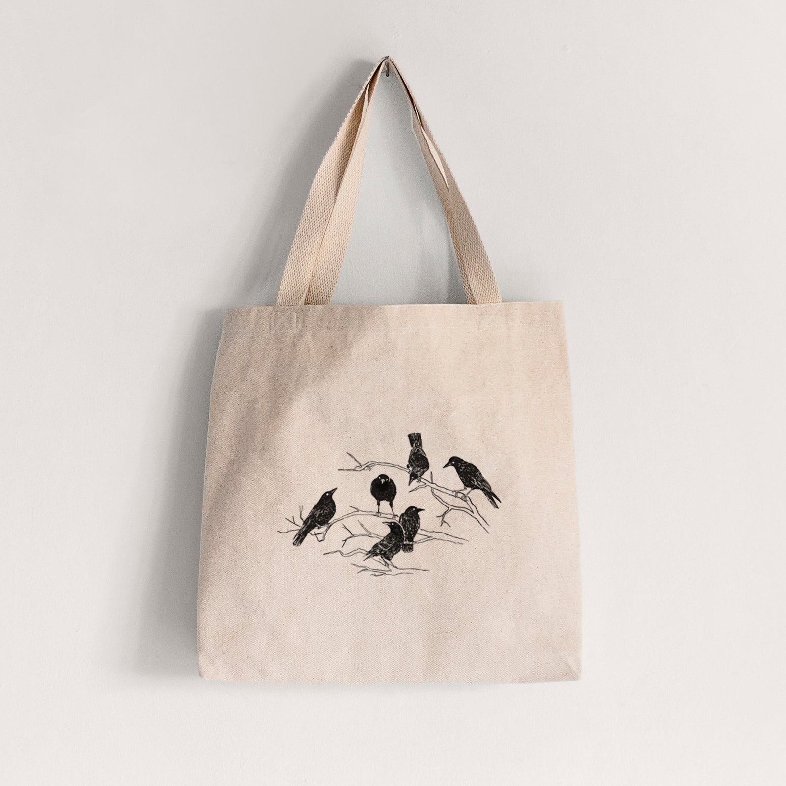 Natural canvas tote bag printed with a black ink illustration of a group of crows perched on bare branches.