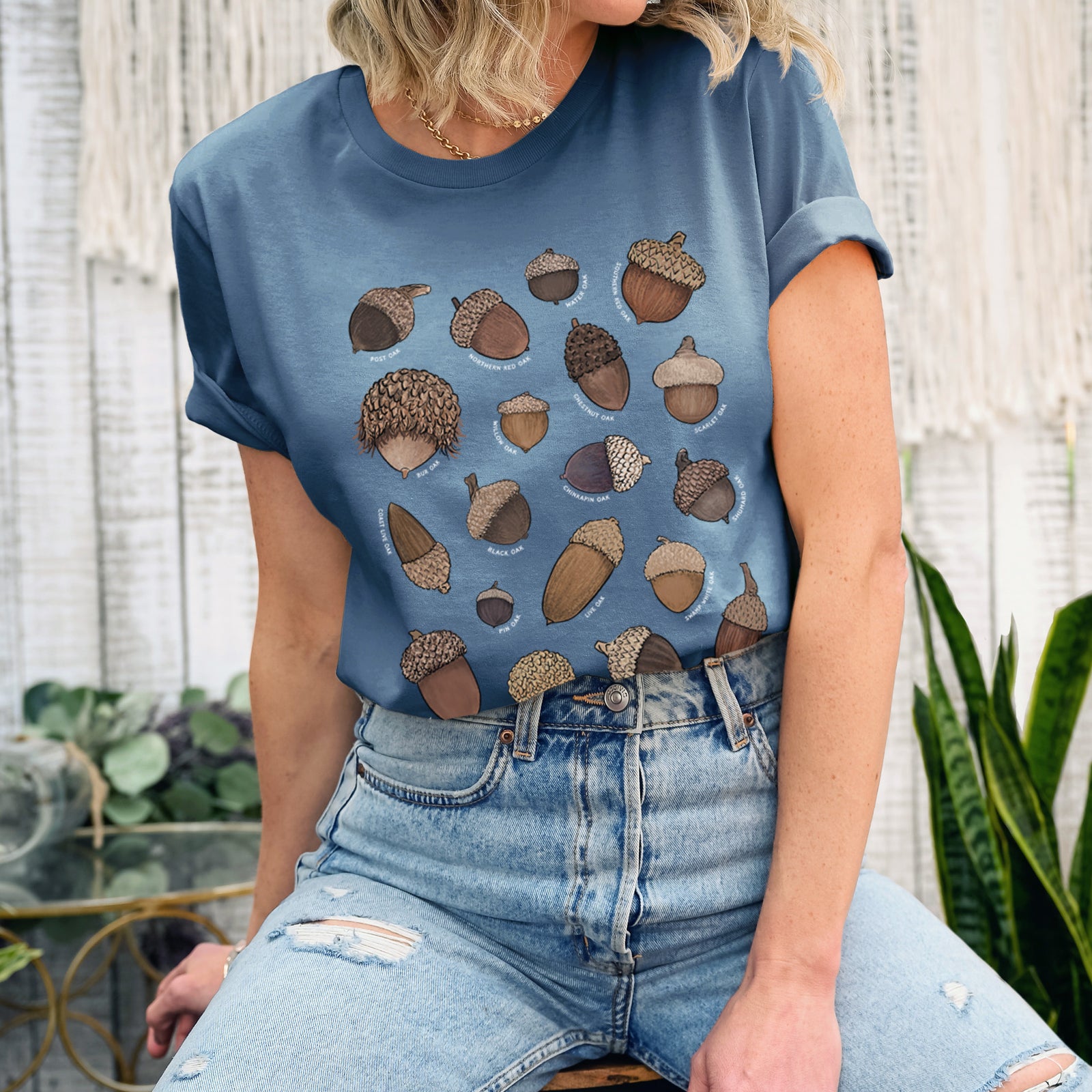 Autumn lightweight cotton t-shirt laid flat, printed with a full-color chart of North American acorns, each labeled with its oak species.