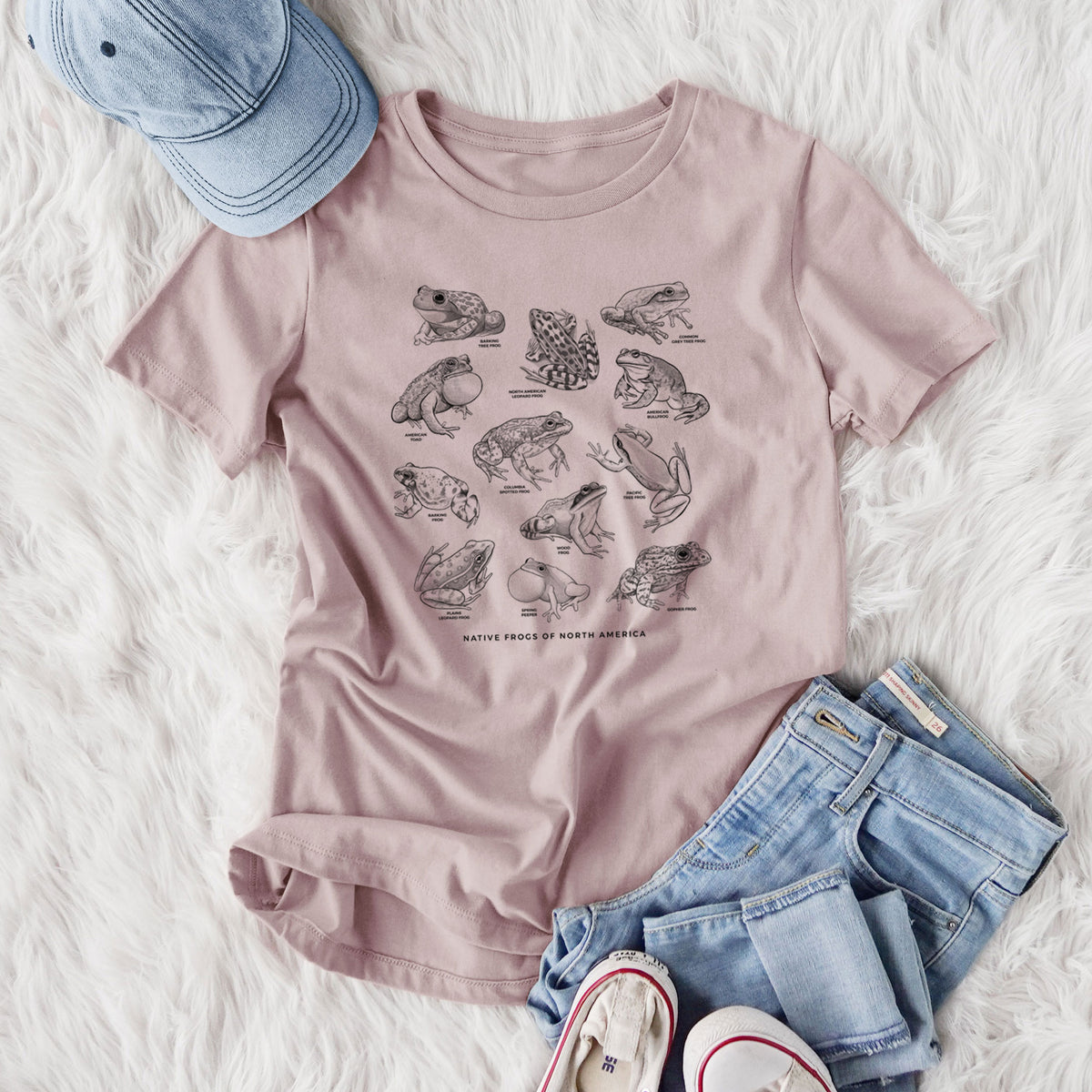 Women's relaxed fit cotton t-shirt printed with a chart of black ink illustrations of North American frog species, styled flat on a white faux fur rug with jeans.