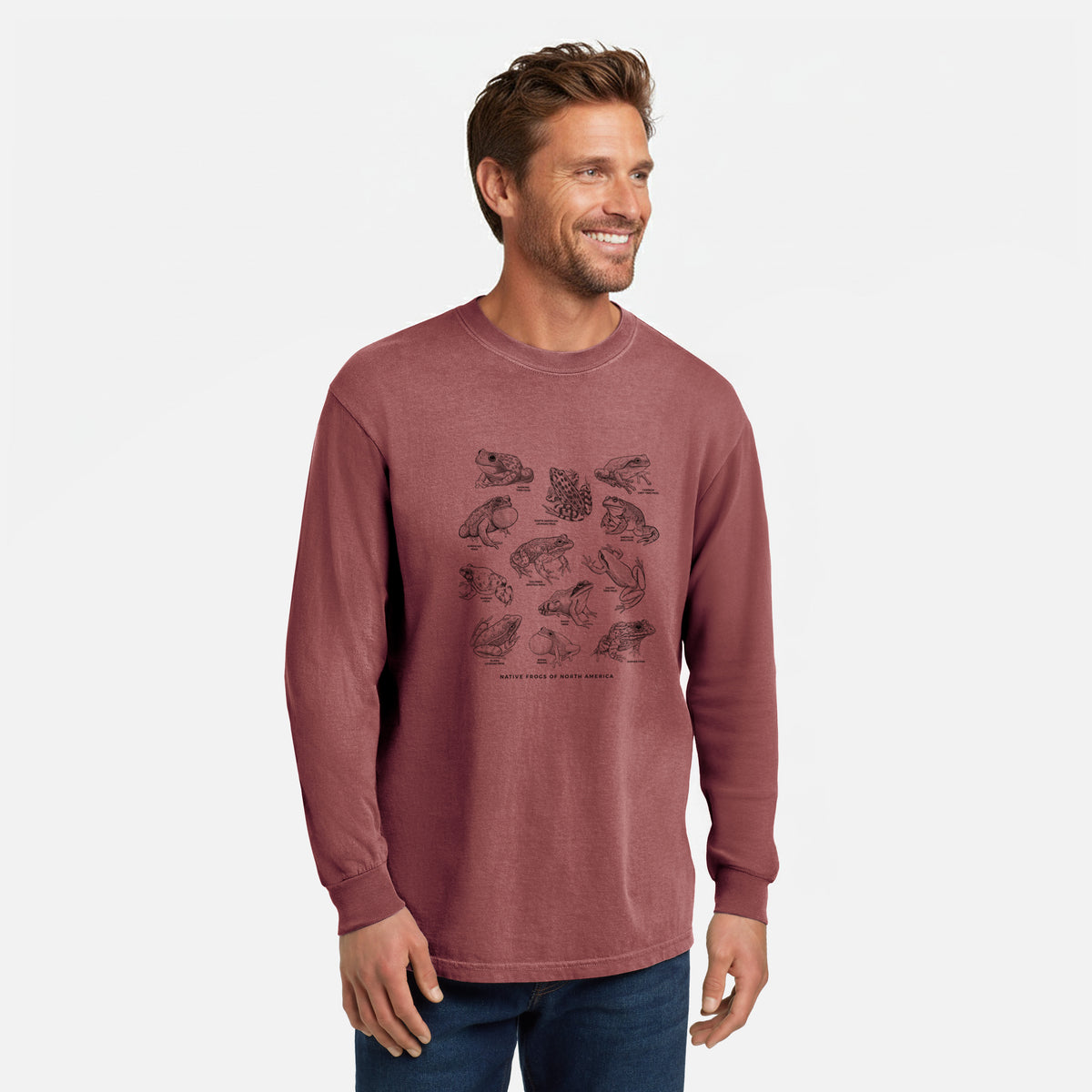 Brick red Comfort Colors long sleeve shirt printed with a chart of black ink illustrations of North American frog species, shown in a lifestyle photo.