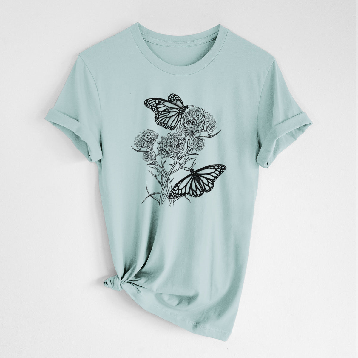 Dusty blue lightweight cotton t-shirt laid flat with the sleeves rolled, printed with a black ink illustration of two monarch butterflies on flowering milkweed.