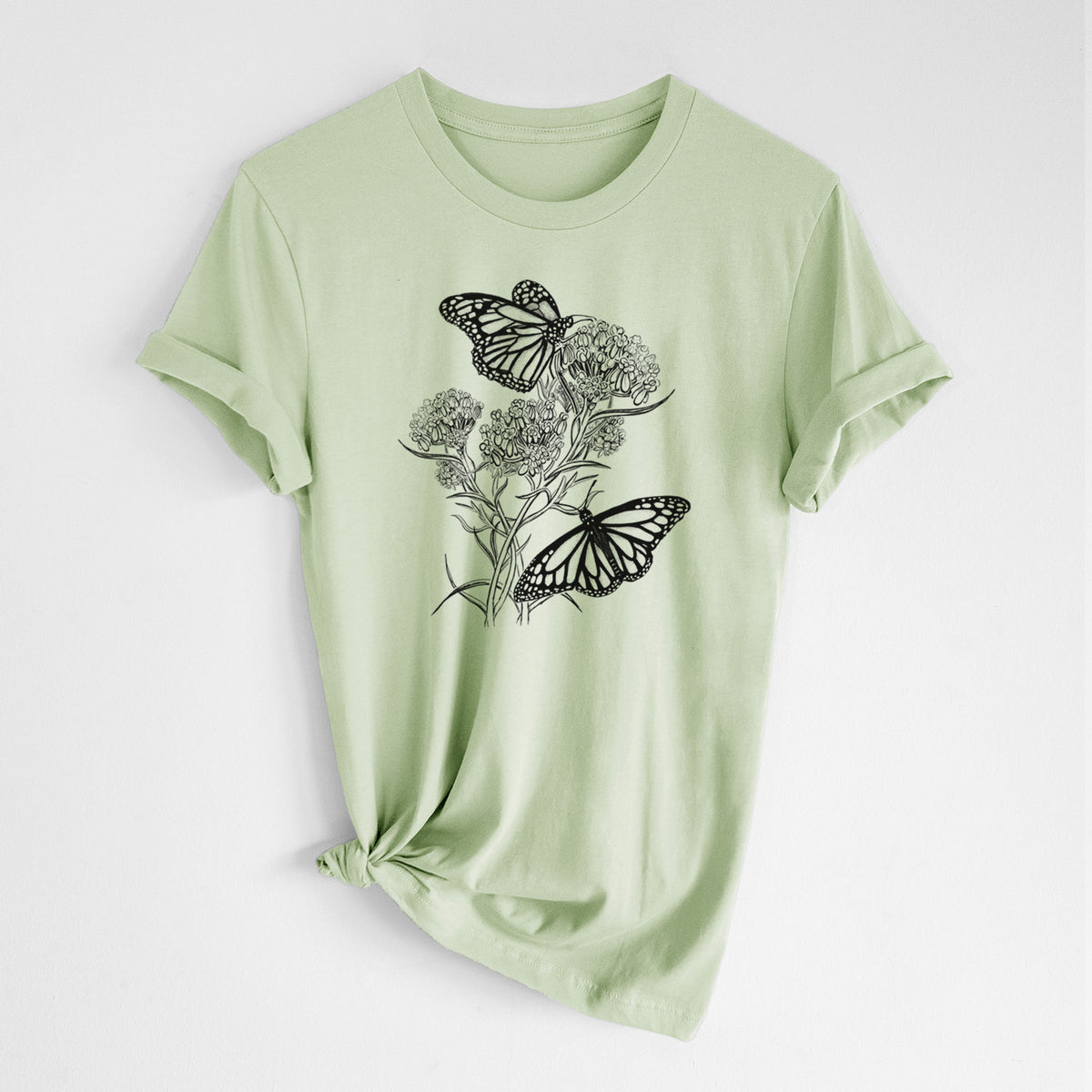 Spring green lightweight cotton t-shirt laid flat with the sleeves rolled, printed with a black ink illustration of two monarch butterflies on flowering milkweed.