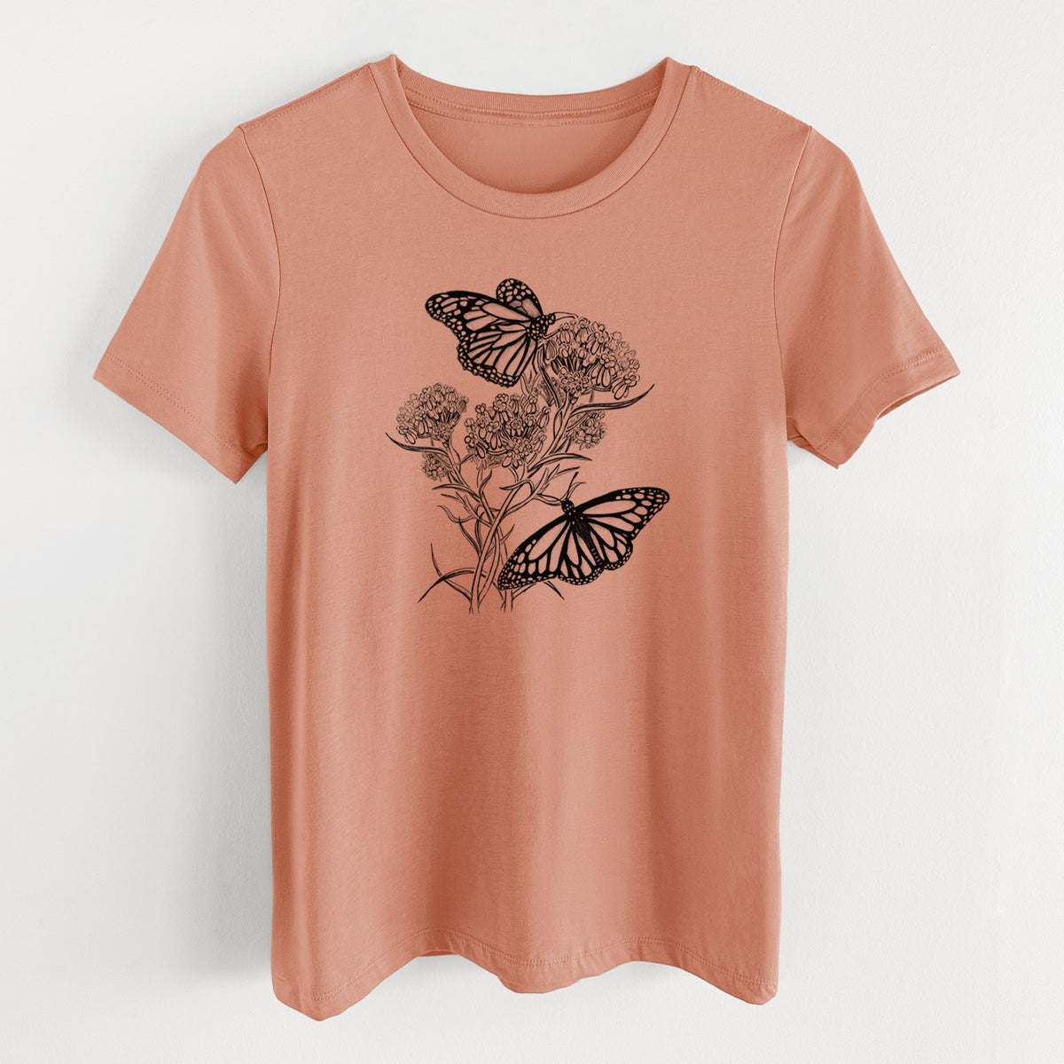 Terracotta orange women's relaxed fit cotton t-shirt laid flat, printed with a black ink illustration of two monarch butterflies on flowering milkweed.