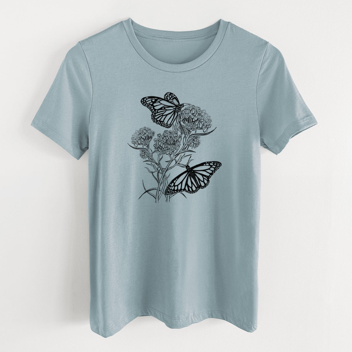 Vintage denim women's relaxed fit cotton t-shirt laid flat, printed with a black ink illustration of two monarch butterflies on flowering milkweed.