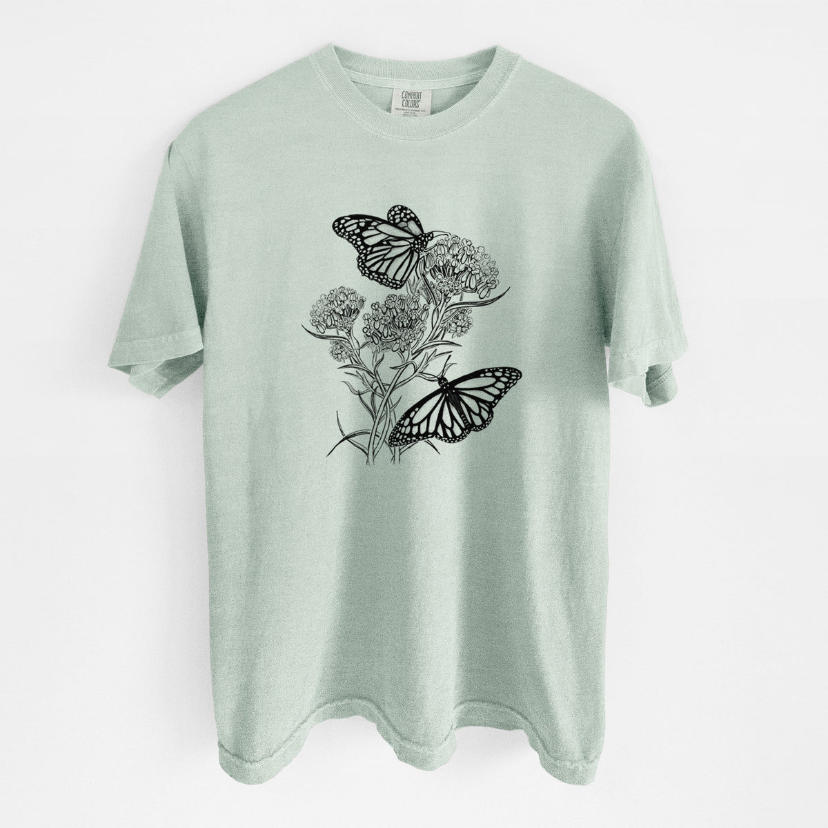 Bay green Comfort Colors t-shirt laid flat, printed with a black ink illustration of two monarch butterflies on flowering milkweed.