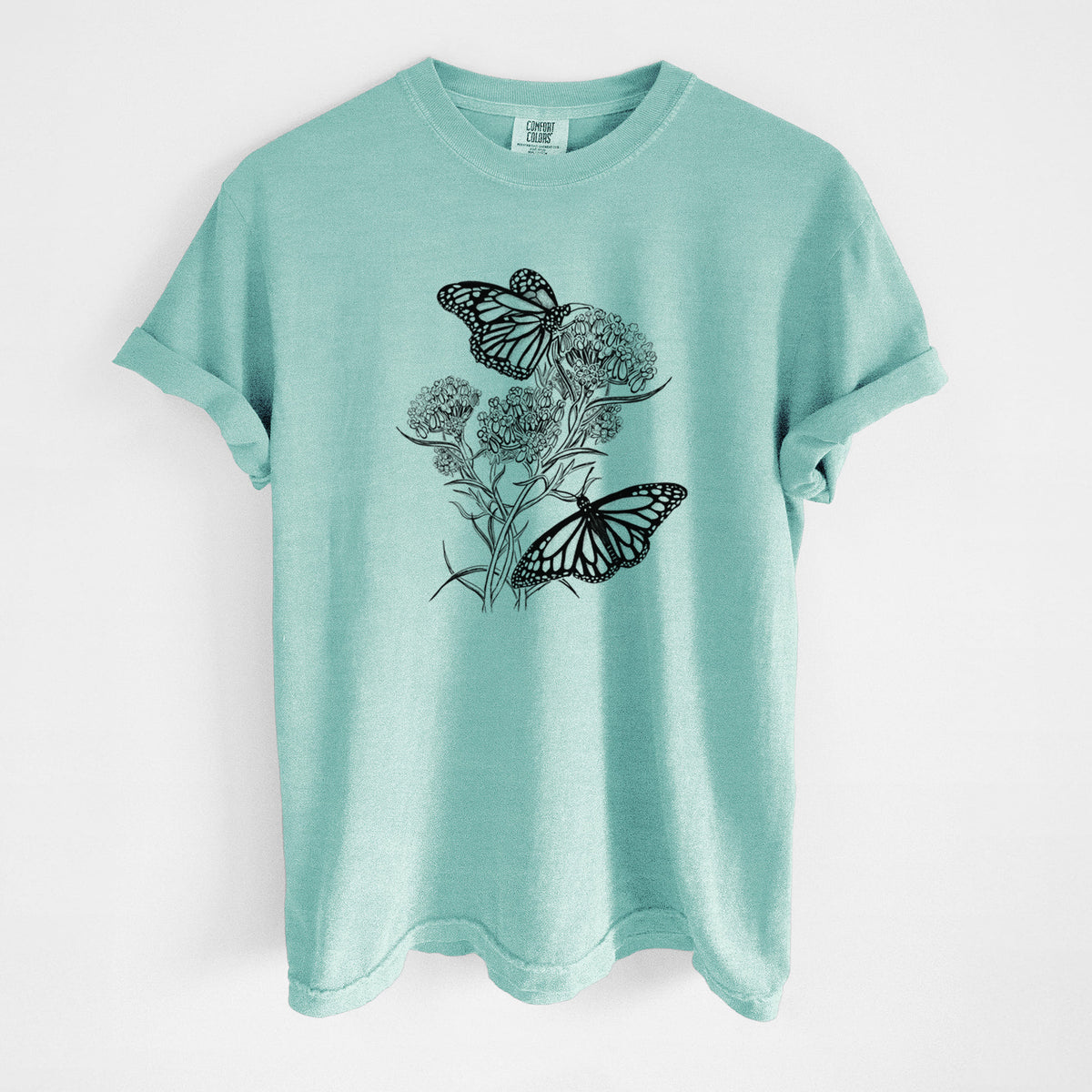 Chalky mint Comfort Colors t-shirt laid flat, printed with a black ink illustration of two monarch butterflies on flowering milkweed.