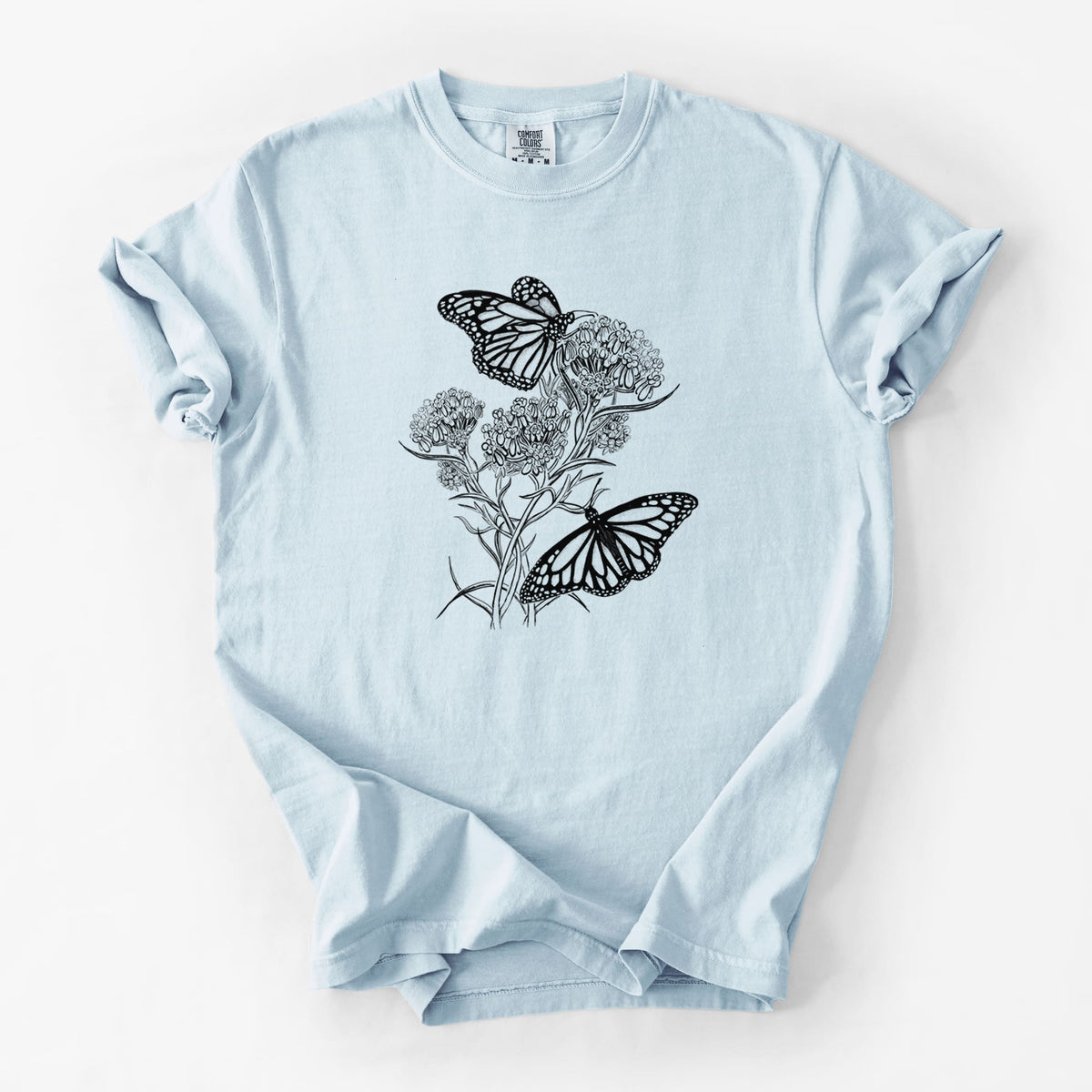 Chambray blue Comfort Colors t-shirt laid flat, printed with a black ink illustration of two monarch butterflies on flowering milkweed.