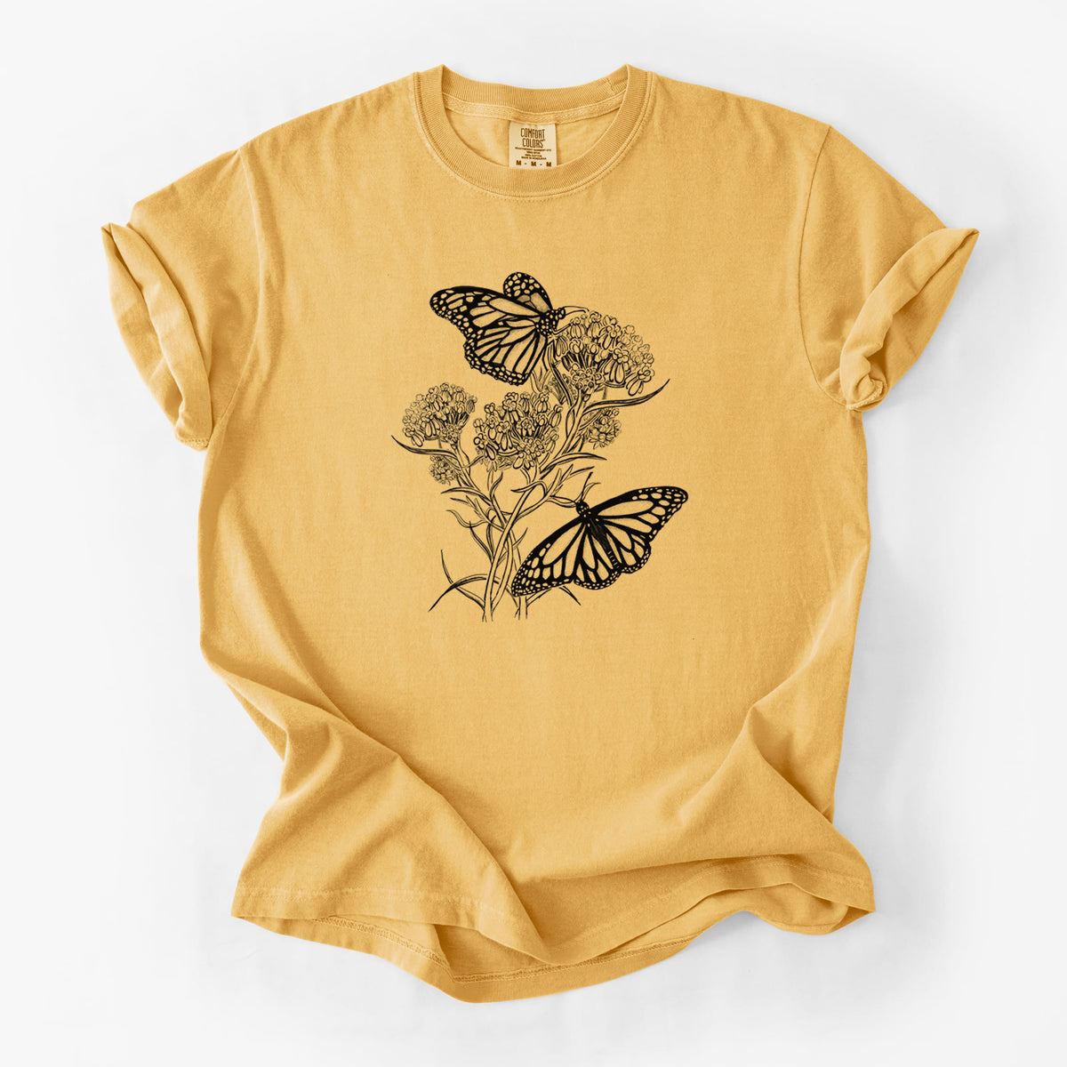 Golden wheat yellow Comfort Colors t-shirt laid flat, printed with a black ink illustration of two monarch butterflies on flowering milkweed.