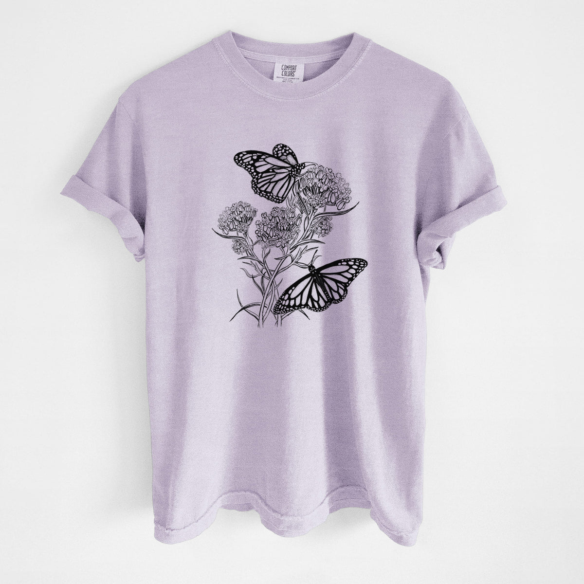Orchid purple Comfort Colors t-shirt laid flat, printed with a black ink illustration of two monarch butterflies on flowering milkweed.