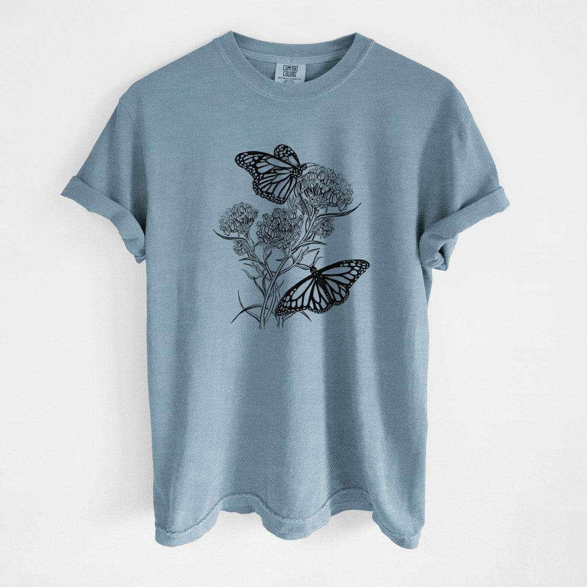 Steel blue Comfort Colors t-shirt laid flat, printed with a black ink illustration of two monarch butterflies on flowering milkweed.
