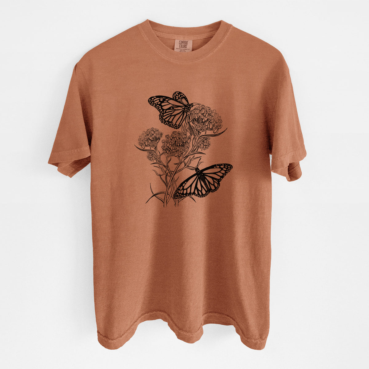 Yam burnt orange Comfort Colors t-shirt laid flat, printed with a black ink illustration of two monarch butterflies on flowering milkweed.