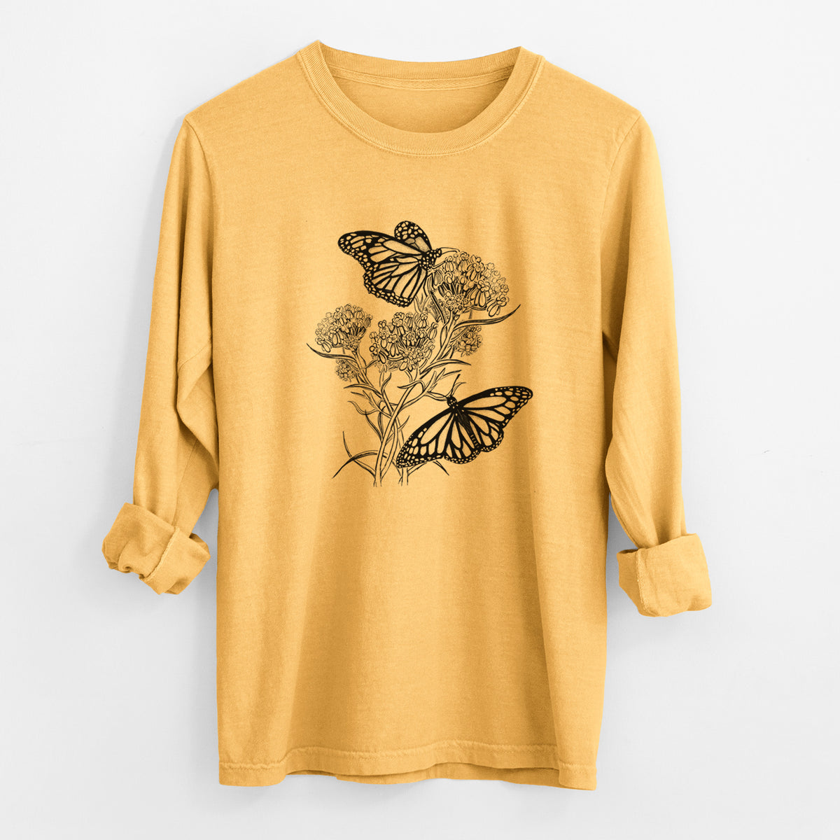 Golden wheat yellow Comfort Colors long sleeve shirt laid flat with the cuffs rolled, printed with a black ink illustration of two monarch butterflies on flowering milkweed.