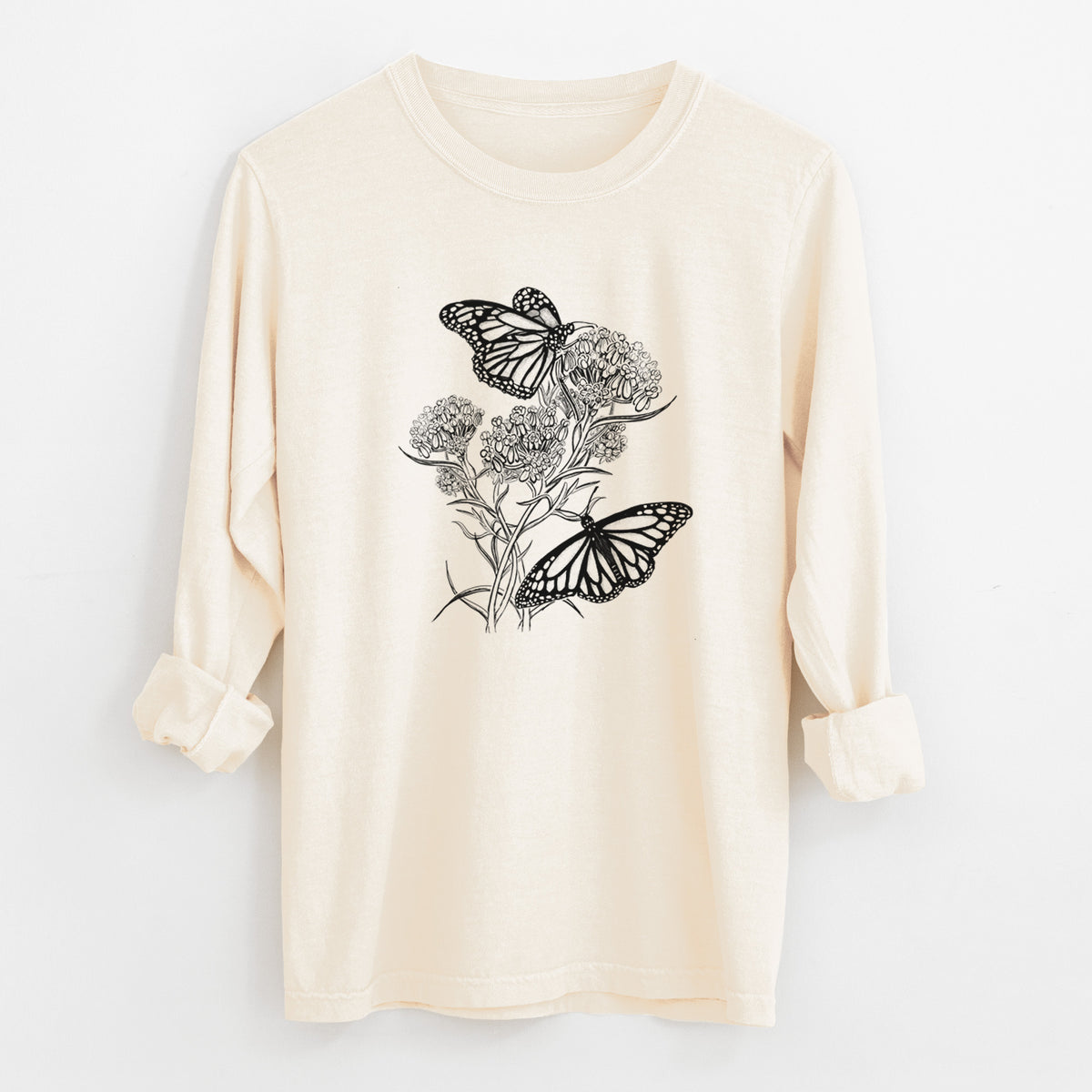 Ivory Comfort Colors long sleeve shirt laid flat with the cuffs rolled, printed with a black ink illustration of two monarch butterflies on flowering milkweed.