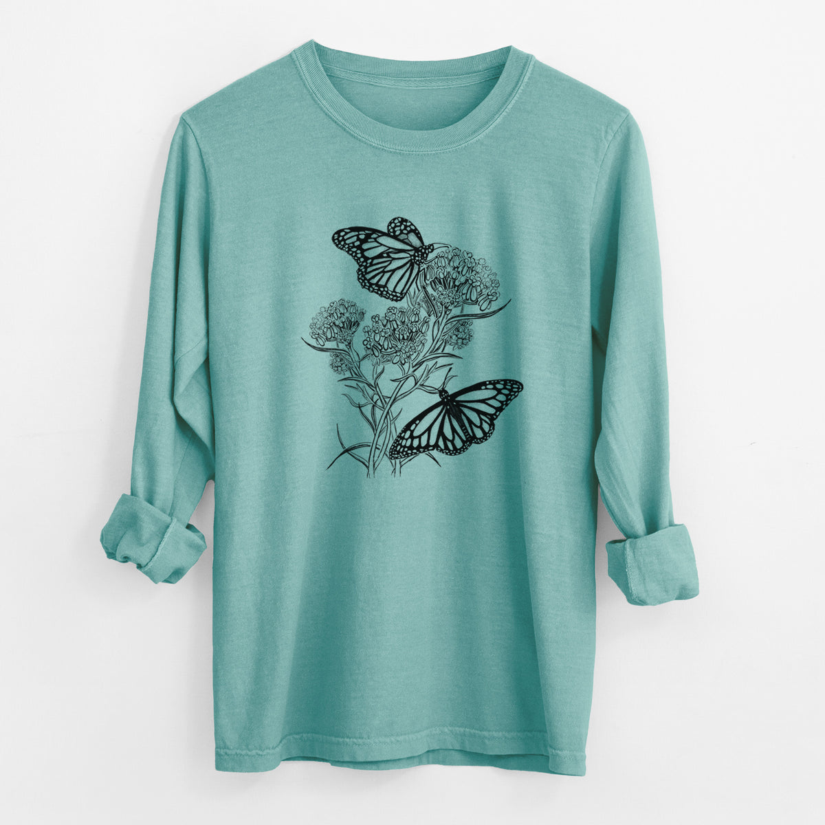 Reef green Comfort Colors long sleeve shirt laid flat with the cuffs rolled, printed with a black ink illustration of two monarch butterflies on flowering milkweed.