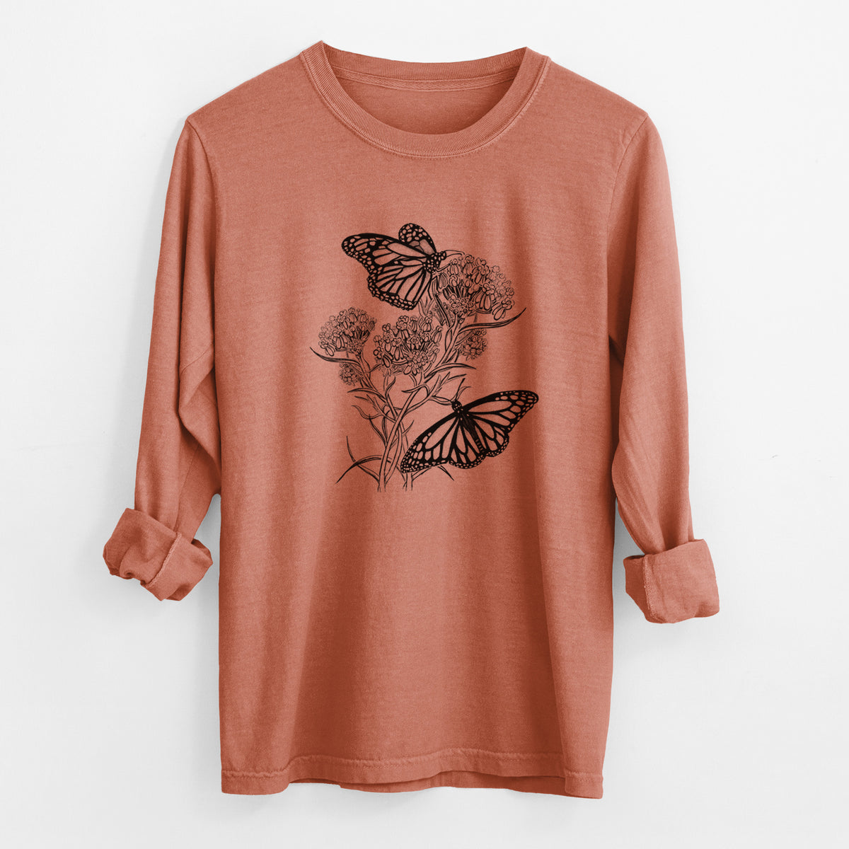 Yam burnt orange Comfort Colors long sleeve shirt laid flat with the cuffs rolled, printed with a black ink illustration of two monarch butterflies on flowering milkweed.
