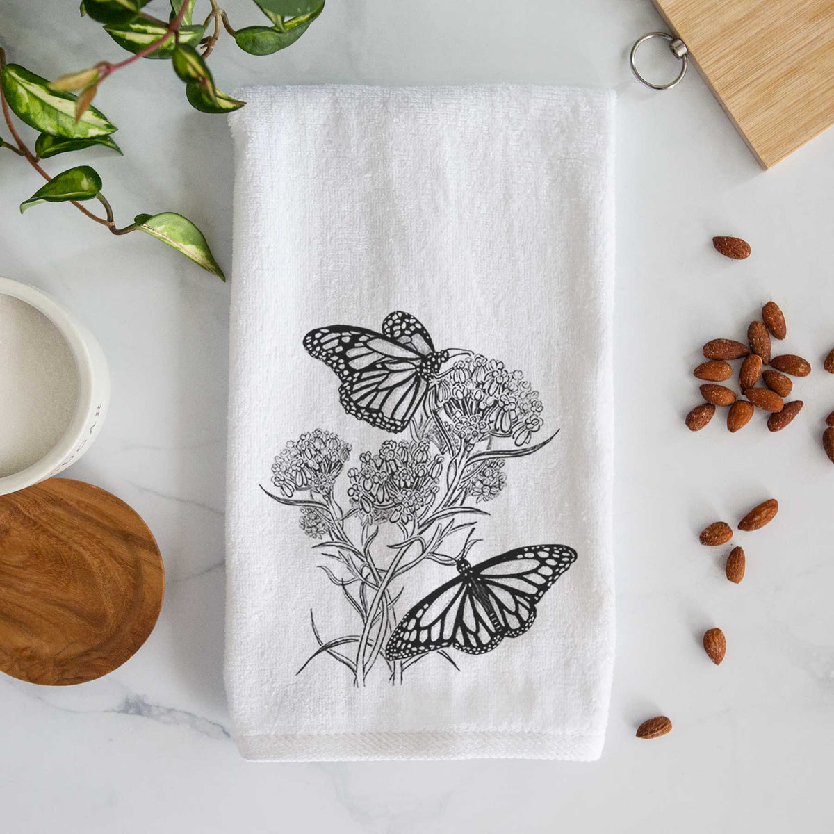 White hand towel printed with a black ink illustration of two monarch butterflies on flowering milkweed.