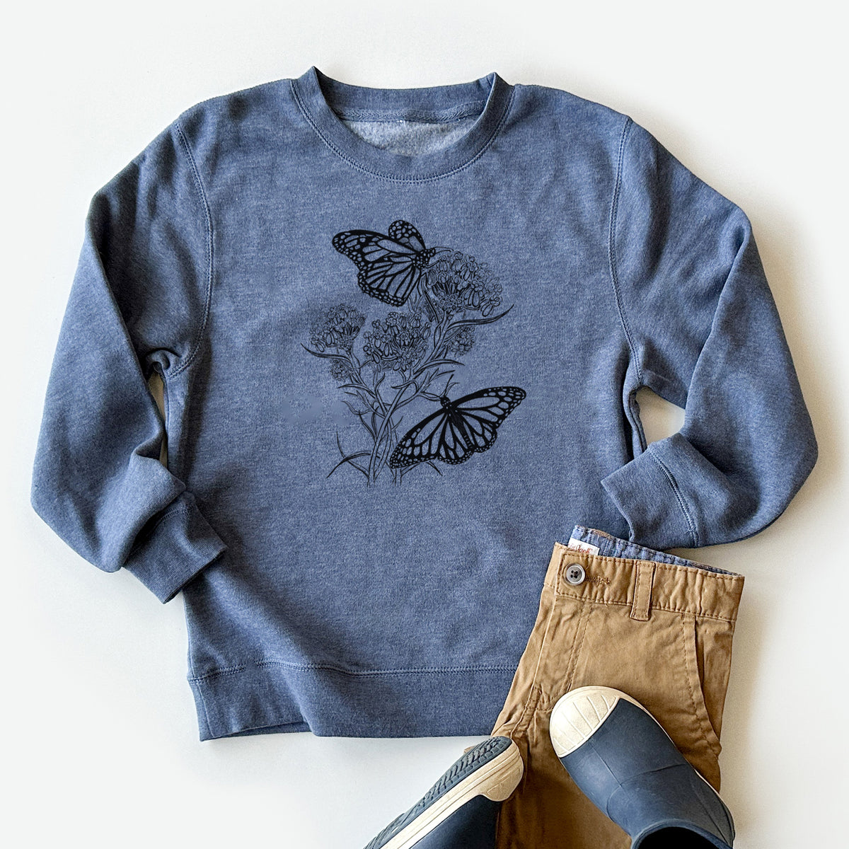 Youth crewneck sweatshirt printed with a black ink illustration of two monarch butterflies on flowering milkweed, styled flat with khaki pants and shoes.