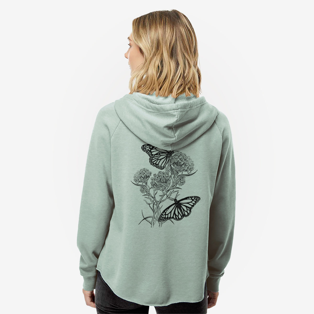 Woman wearing a sage green women's Cali Wave zip-up sweatshirt printed with a black ink illustration of two monarch butterflies on flowering milkweed, seen from behind.