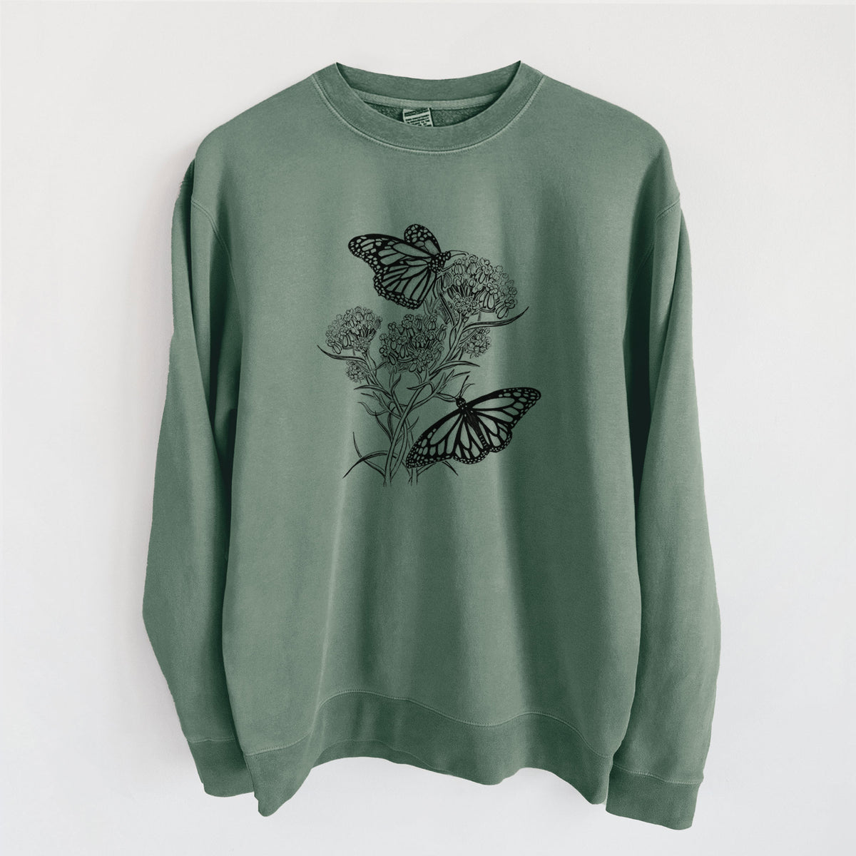 Alpine green pigment dyed crewneck sweatshirt laid flat, printed with a black ink illustration of two monarch butterflies on flowering milkweed.