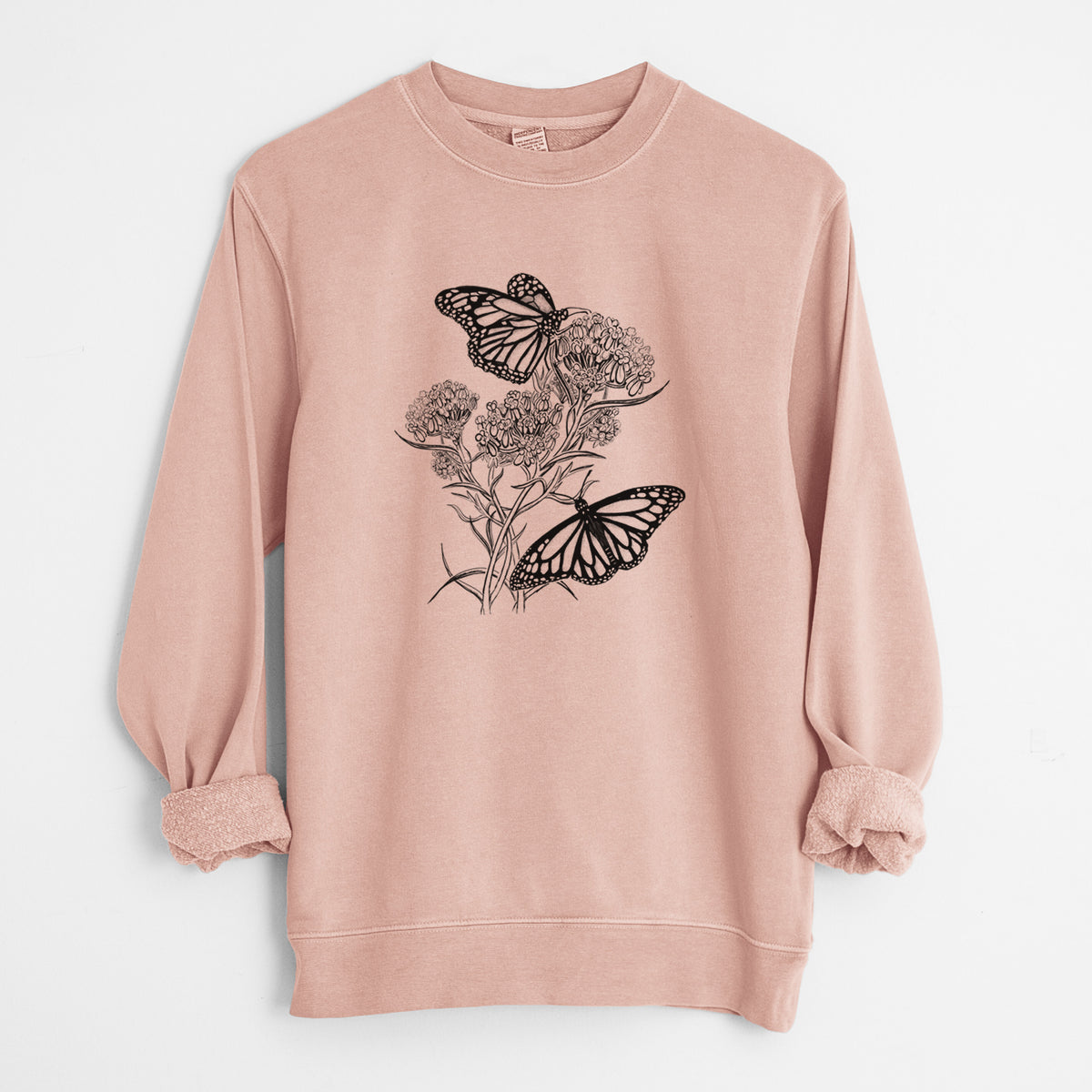 Dusty pink pigment dyed crewneck sweatshirt laid flat with the sleeves rolled, printed with a black ink illustration of two monarch butterflies on flowering milkweed.