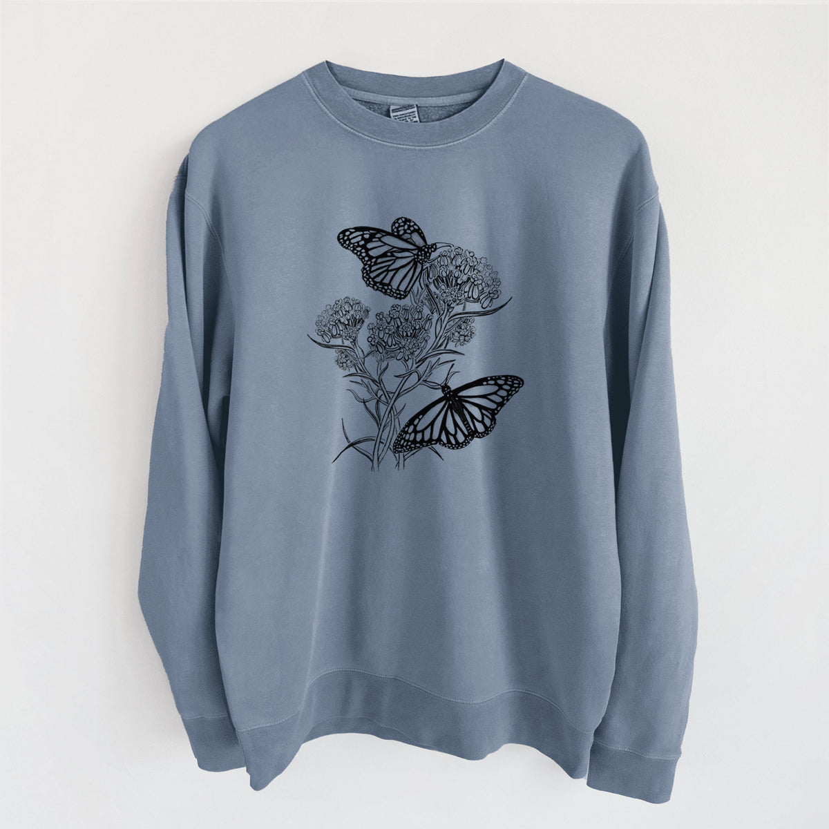 Slate blue pigment dyed crewneck sweatshirt laid flat, printed with a black ink illustration of two monarch butterflies on flowering milkweed.