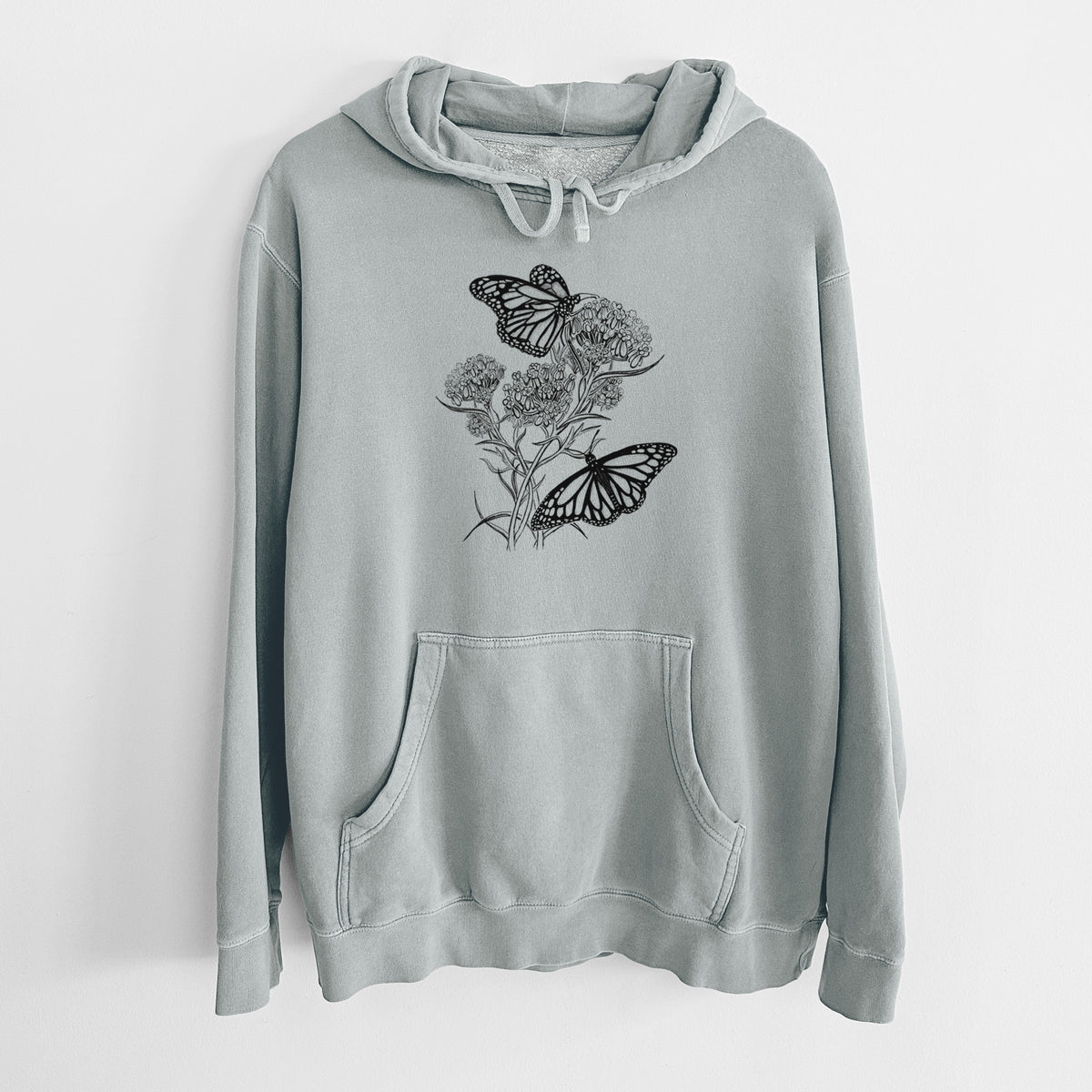 Sage green pigment dyed hoodie laid flat, printed with a black ink illustration of two monarch butterflies on flowering milkweed.