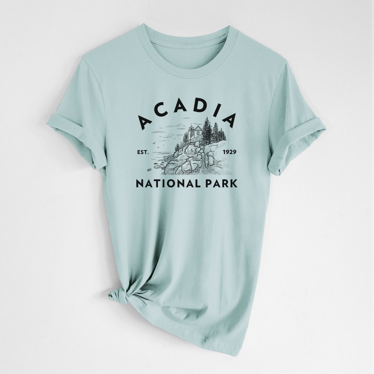 Dusty blue lightweight cotton t-shirt laid flat with the sleeves rolled, printed with a round badge of a rocky coastline and pine trees, with the words Acadia National Park, Est. 1929.