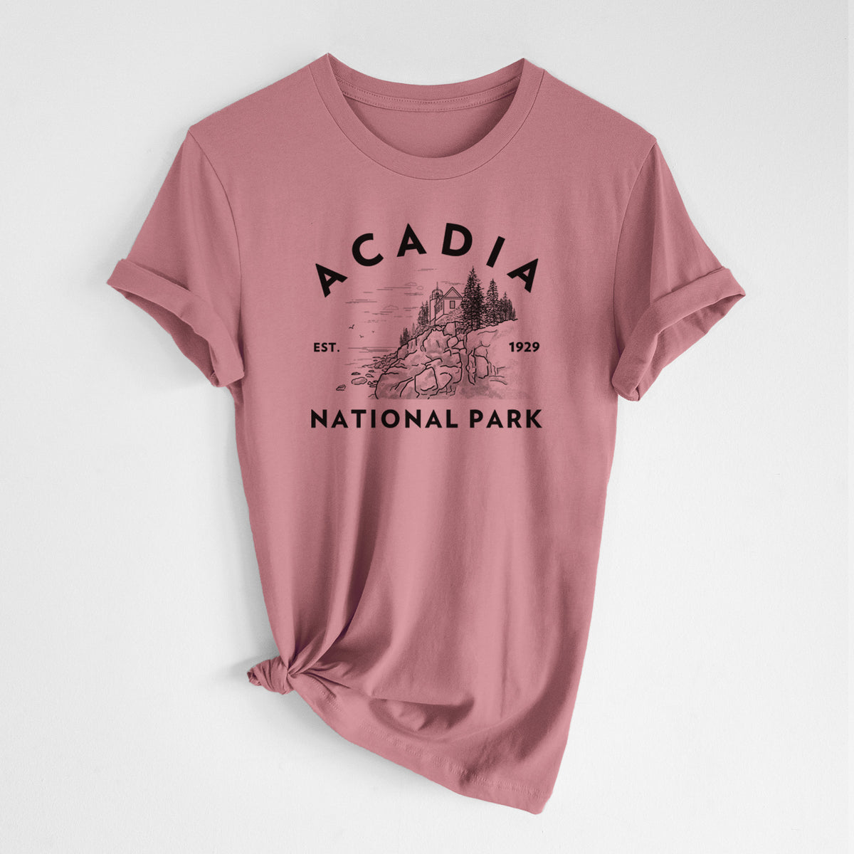 Mauve pink lightweight cotton t-shirt laid flat with the sleeves rolled, printed with a round badge of a rocky coastline and pine trees, with the words Acadia National Park, Est. 1929.
