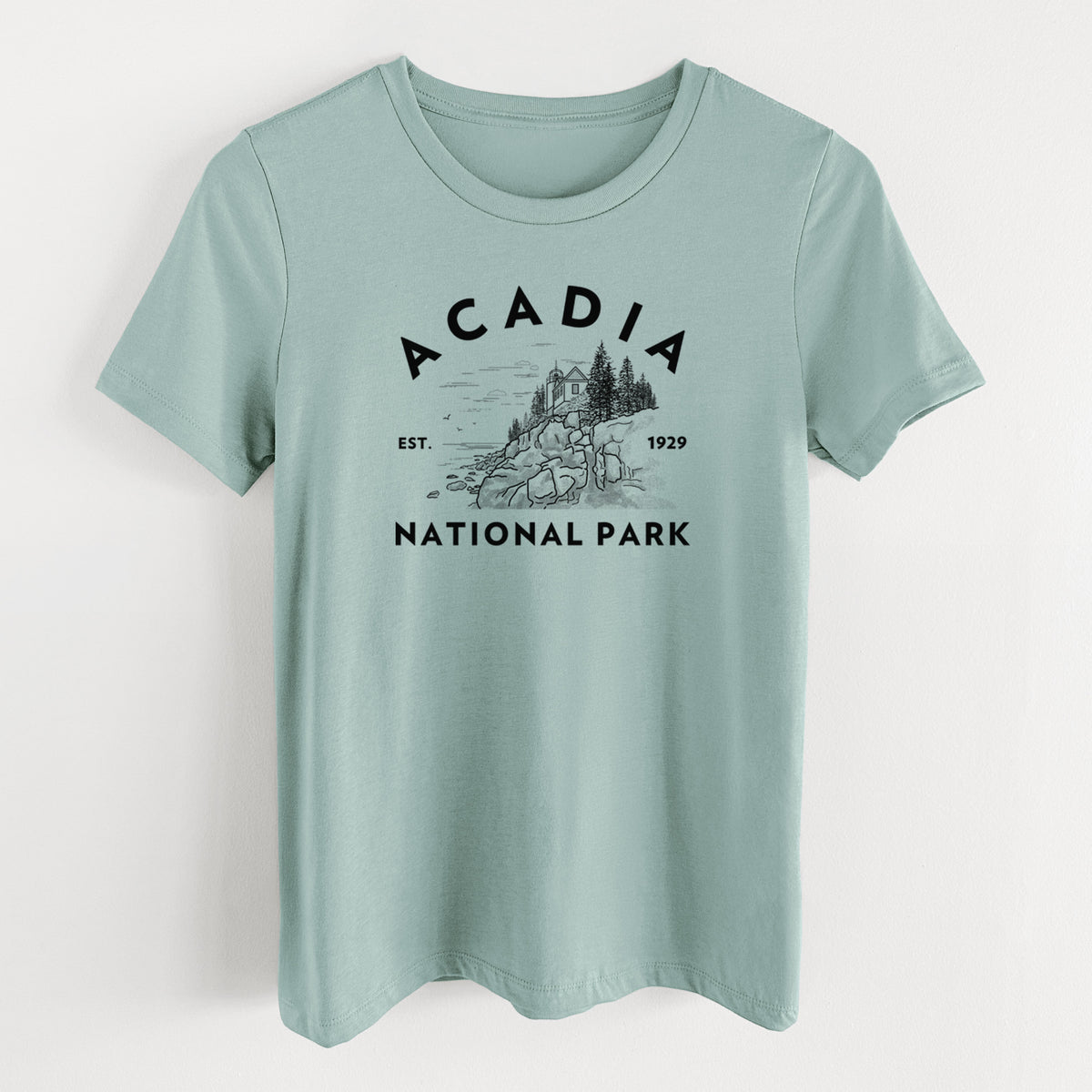Dusty blue women's relaxed fit cotton t-shirt laid flat, printed with a round badge of a rocky coastline and pine trees, with the words Acadia National Park, Est. 1929.