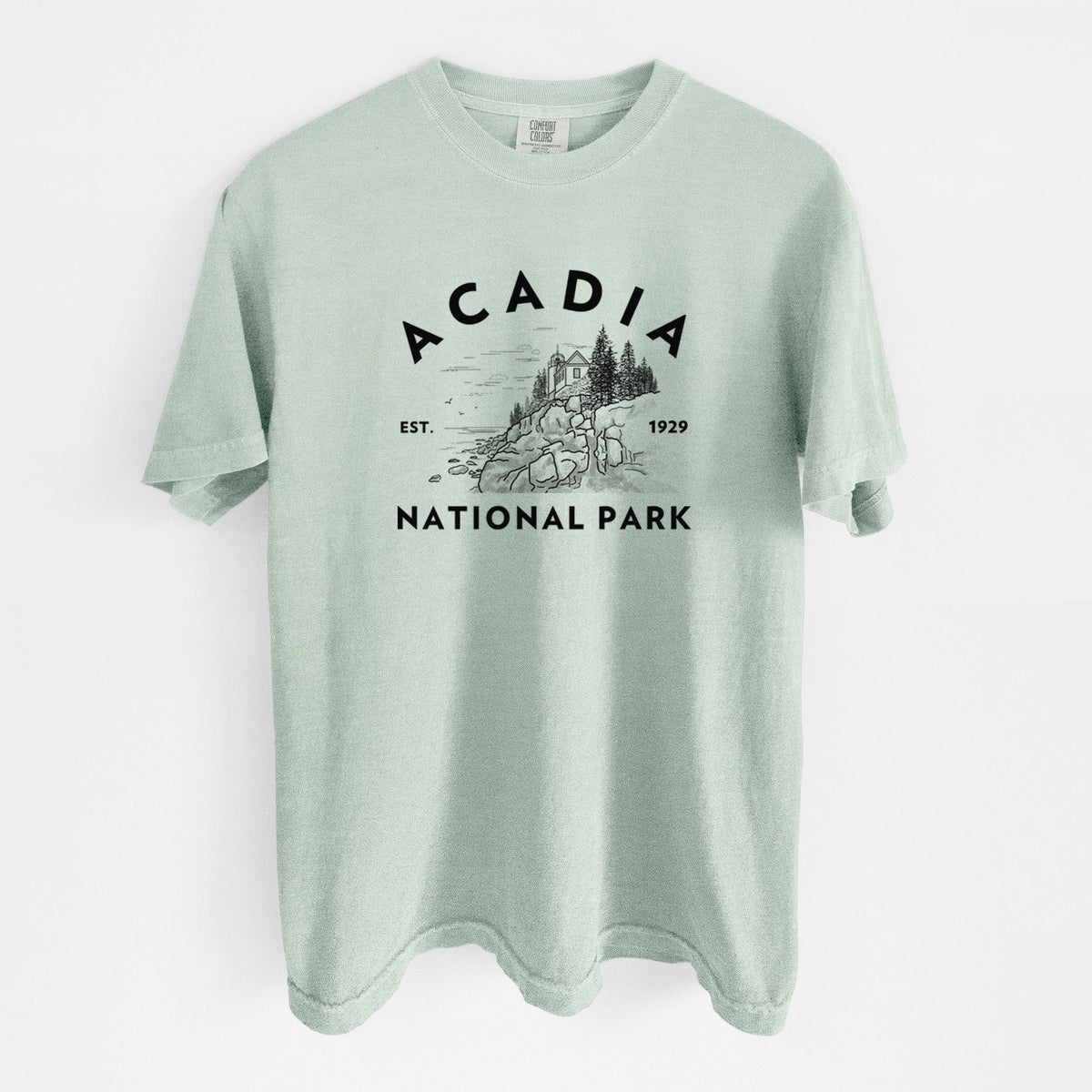 Bay green Comfort Colors t-shirt laid flat, printed with a round badge of a rocky coastline and pine trees, with the words Acadia National Park, Est. 1929.