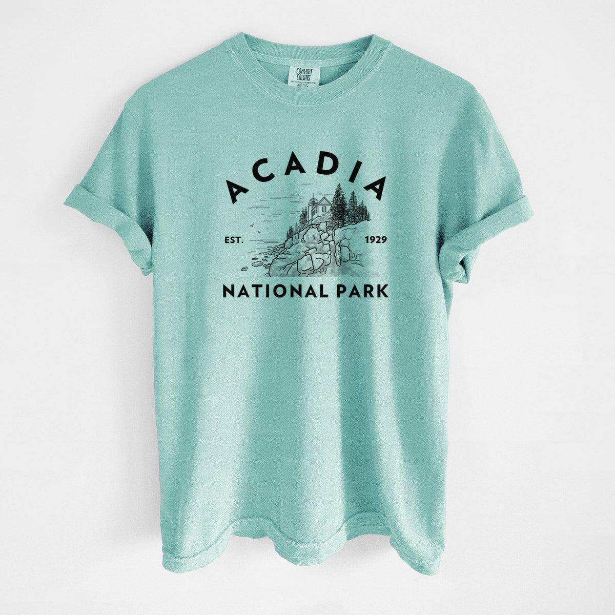 Chalky mint Comfort Colors t-shirt laid flat, printed with a round badge of a rocky coastline and pine trees, with the words Acadia National Park, Est. 1929.