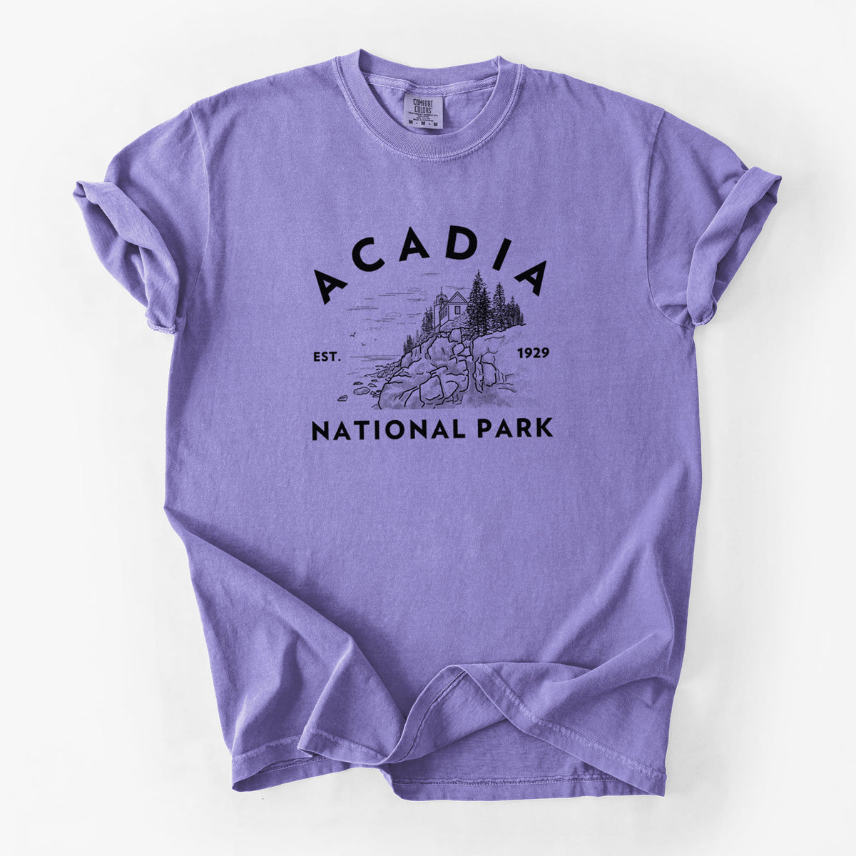 Violet purple Comfort Colors t-shirt laid flat, printed with a round badge of a rocky coastline and pine trees, with the words Acadia National Park, Est. 1929.