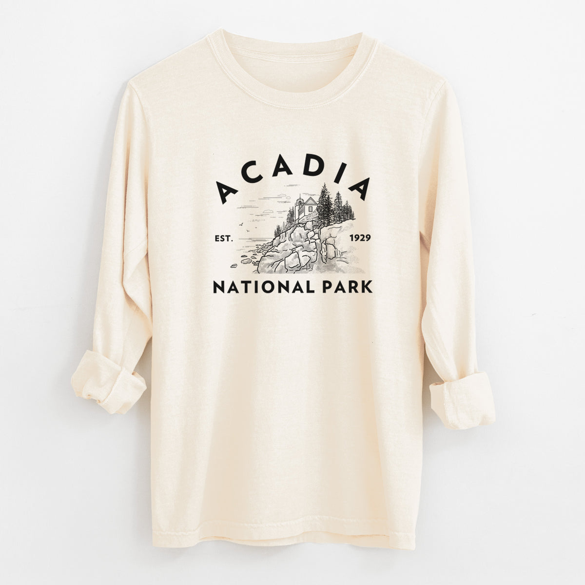 Ivory Comfort Colors long sleeve shirt laid flat with the cuffs rolled, printed with a round badge of a rocky coastline and pine trees, with the words Acadia National Park, Est. 1929.