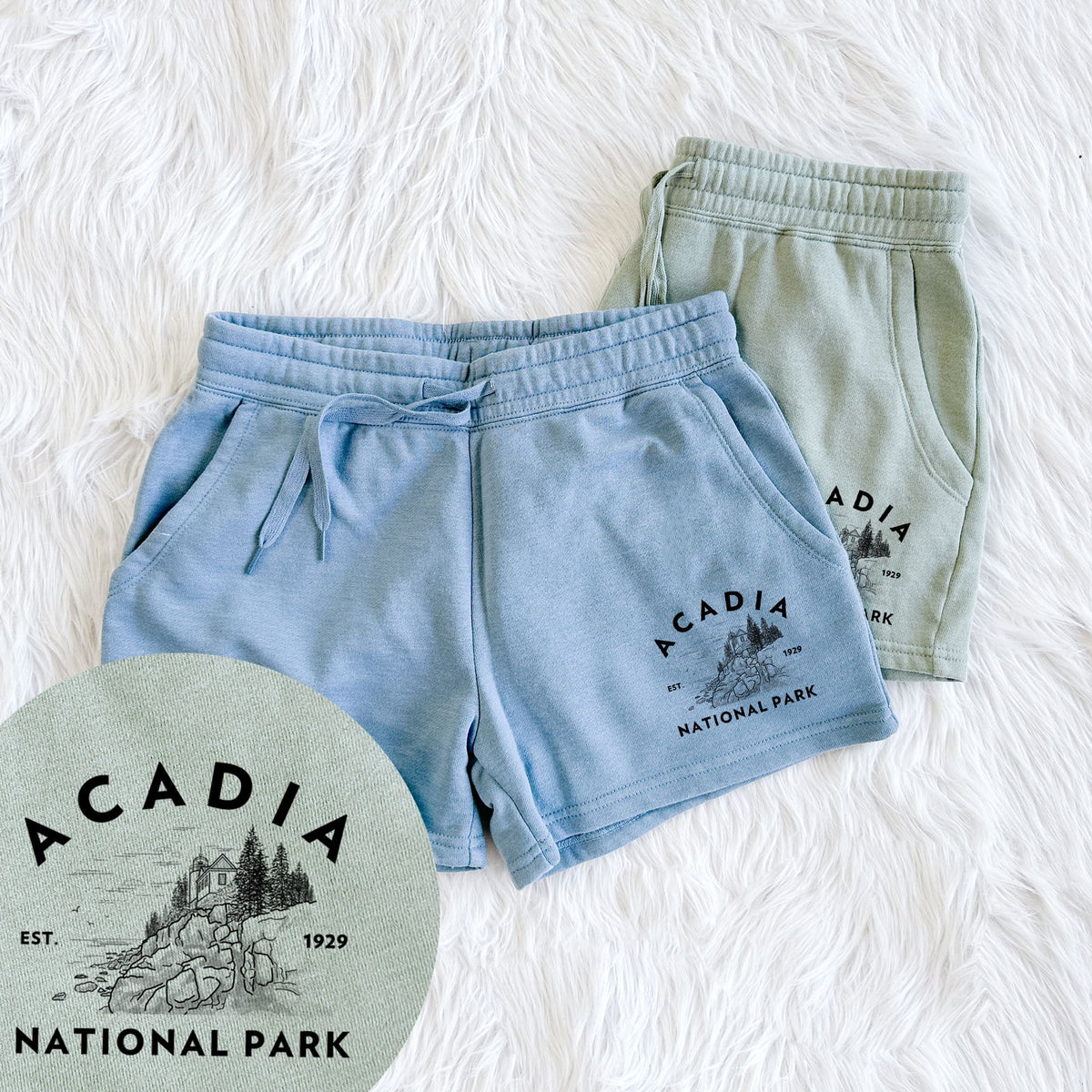 Two pairs of Cali Wave shorts in different colors printed with a round badge of a rocky coastline and pine trees, with the words Acadia National Park, Est. 1929, with a close-up of the print.