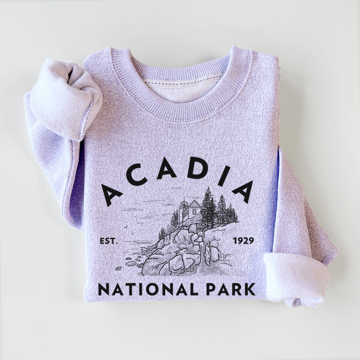 Ice purple knit sweatshirt printed with a round badge of a rocky coastline and pine trees, with the words Acadia National Park, Est. 1929, styled flat.