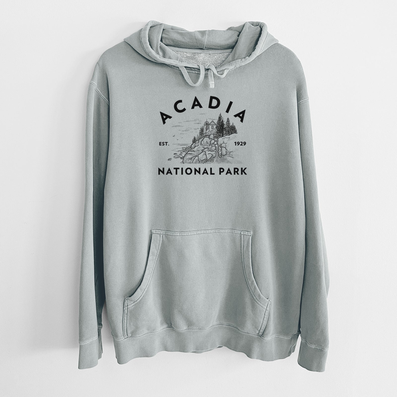 Sage green pigment dyed hoodie laid flat, printed with a round badge of a rocky coastline and pine trees, with the words Acadia National Park, Est. 1929.