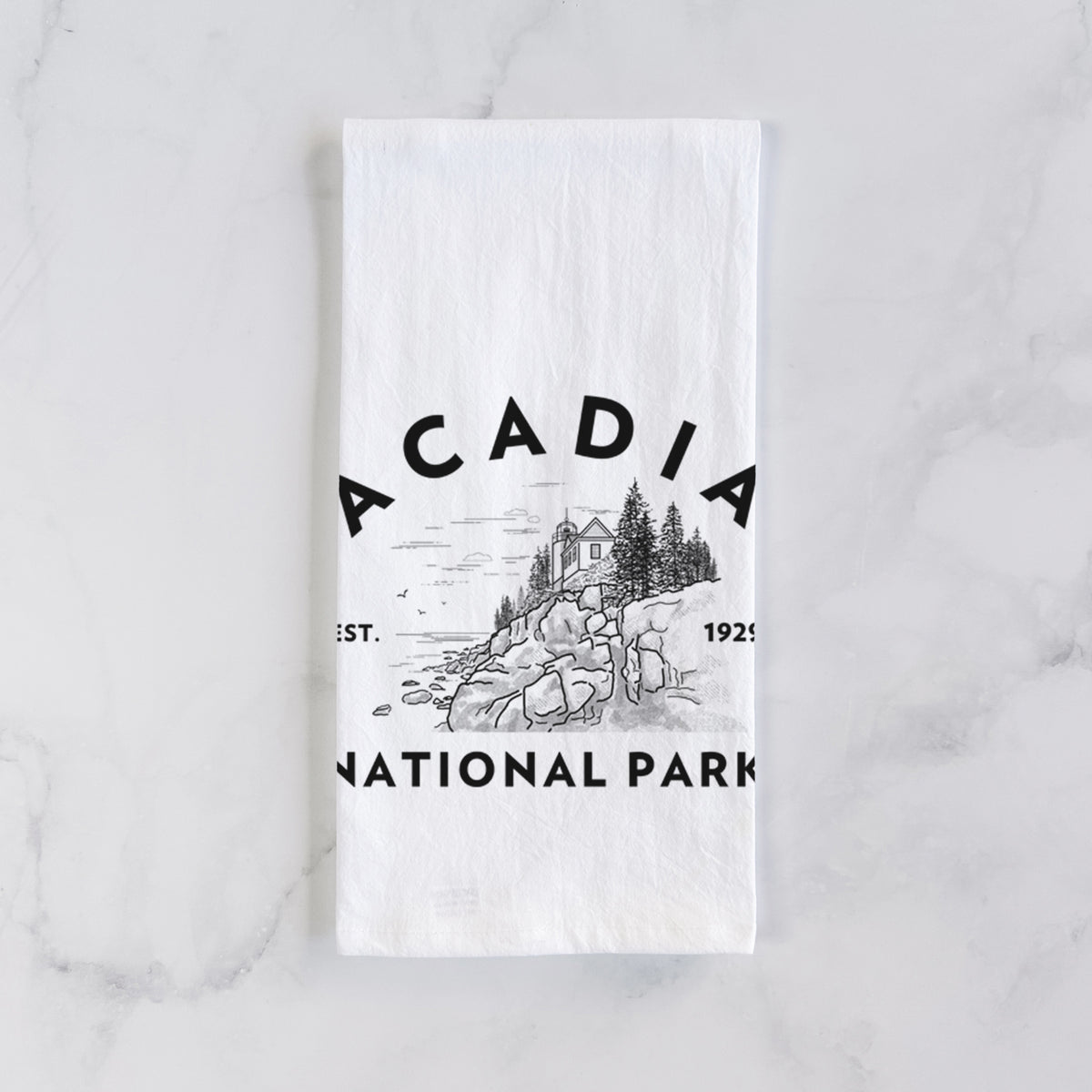White cotton tea towel laid flat on marble, printed with a round badge of a rocky coastline and pine trees, with the words Acadia National Park, Est. 1929.