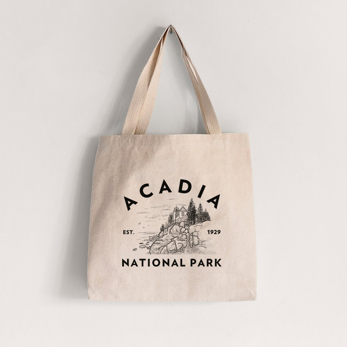 Natural canvas tote bag printed with a round badge of a rocky coastline and pine trees, with the words Acadia National Park, Est. 1929.