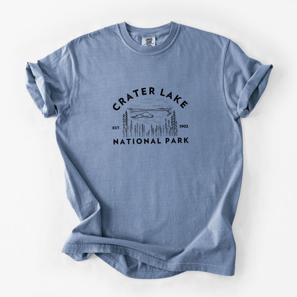 Blue jean Comfort Colors t-shirt laid flat, printed with a round badge of Crater Lake ringed by pine trees, with the words Crater Lake National Park, Est. 1902.