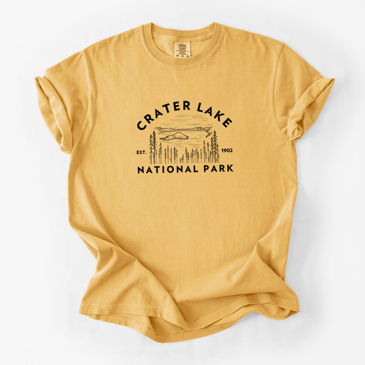 Golden wheat yellow Comfort Colors t-shirt laid flat, printed with a round badge of Crater Lake ringed by pine trees, with the words Crater Lake National Park, Est. 1902.