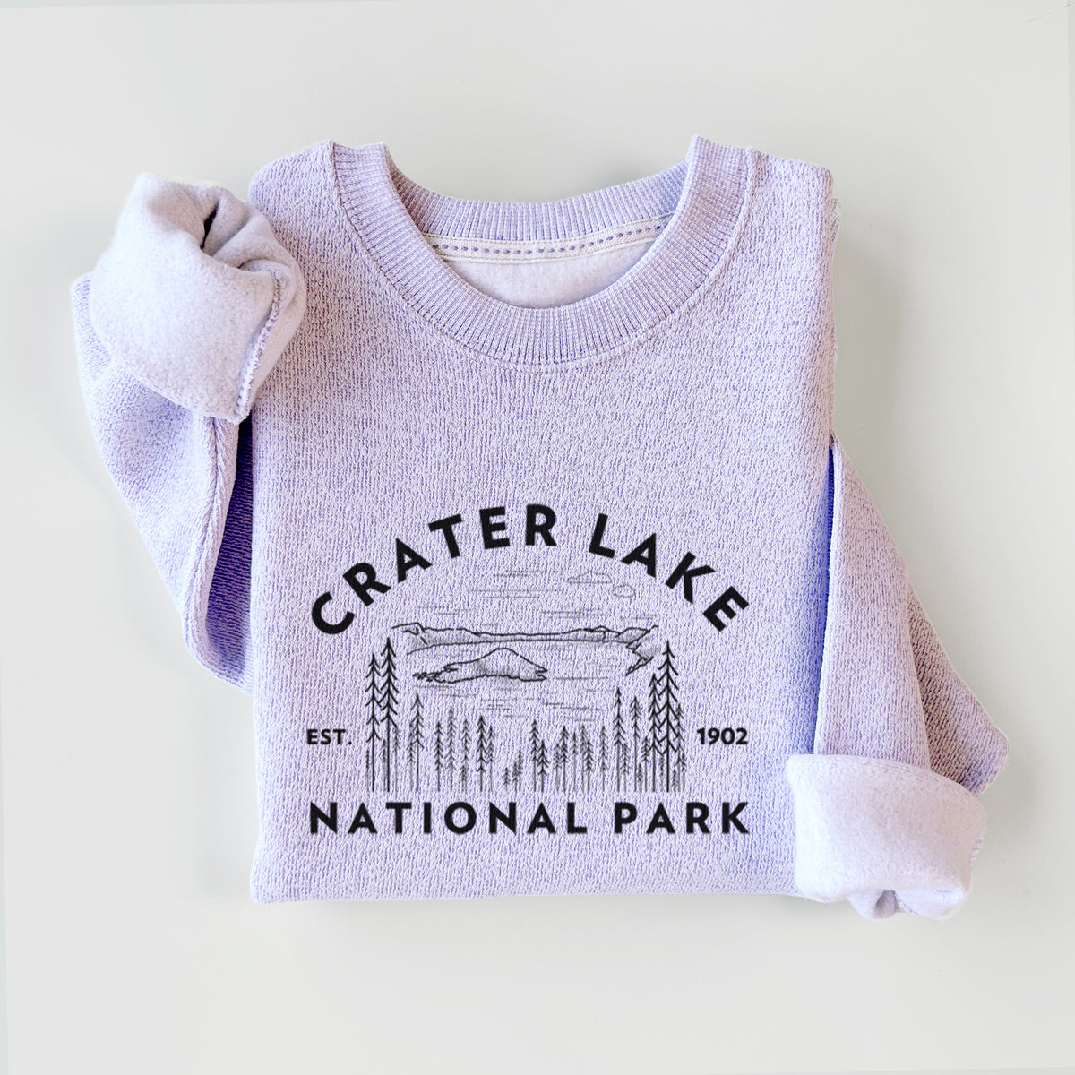 Ice purple knit sweatshirt printed with a round badge of Crater Lake ringed by pine trees, with the words Crater Lake National Park, Est. 1902, styled flat.