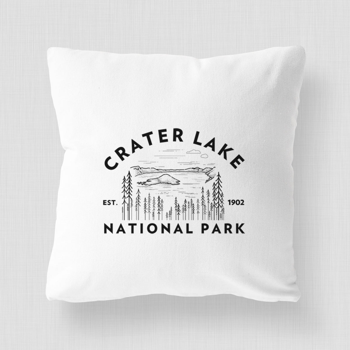 White pillow cover printed with a round badge of Crater Lake ringed by pine trees, with the words Crater Lake National Park, Est. 1902.